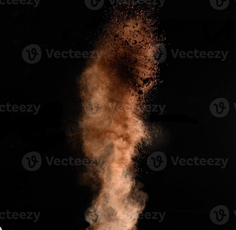 flying brown cocoa particles on a black background. Powder flies up photo