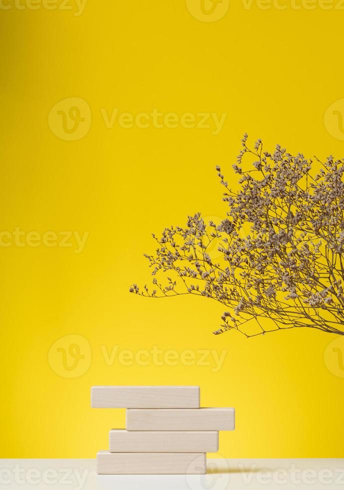 wooden podium to showcase cosmetics and other items, yellow background with dry wildflowers and shadow photo