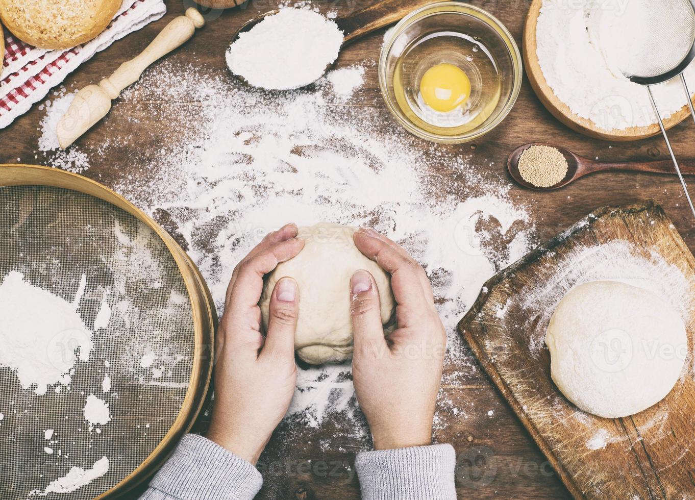 women's hands hold a ball of yeast dough on a table photo