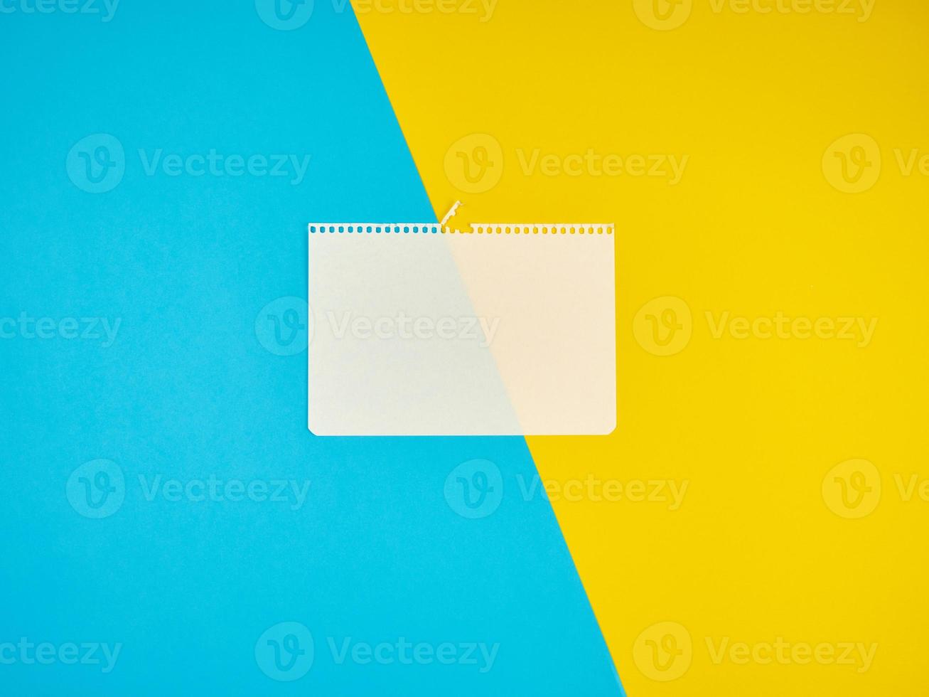 blank white sheet of paper torn from a notebook on a blue-yellow background photo