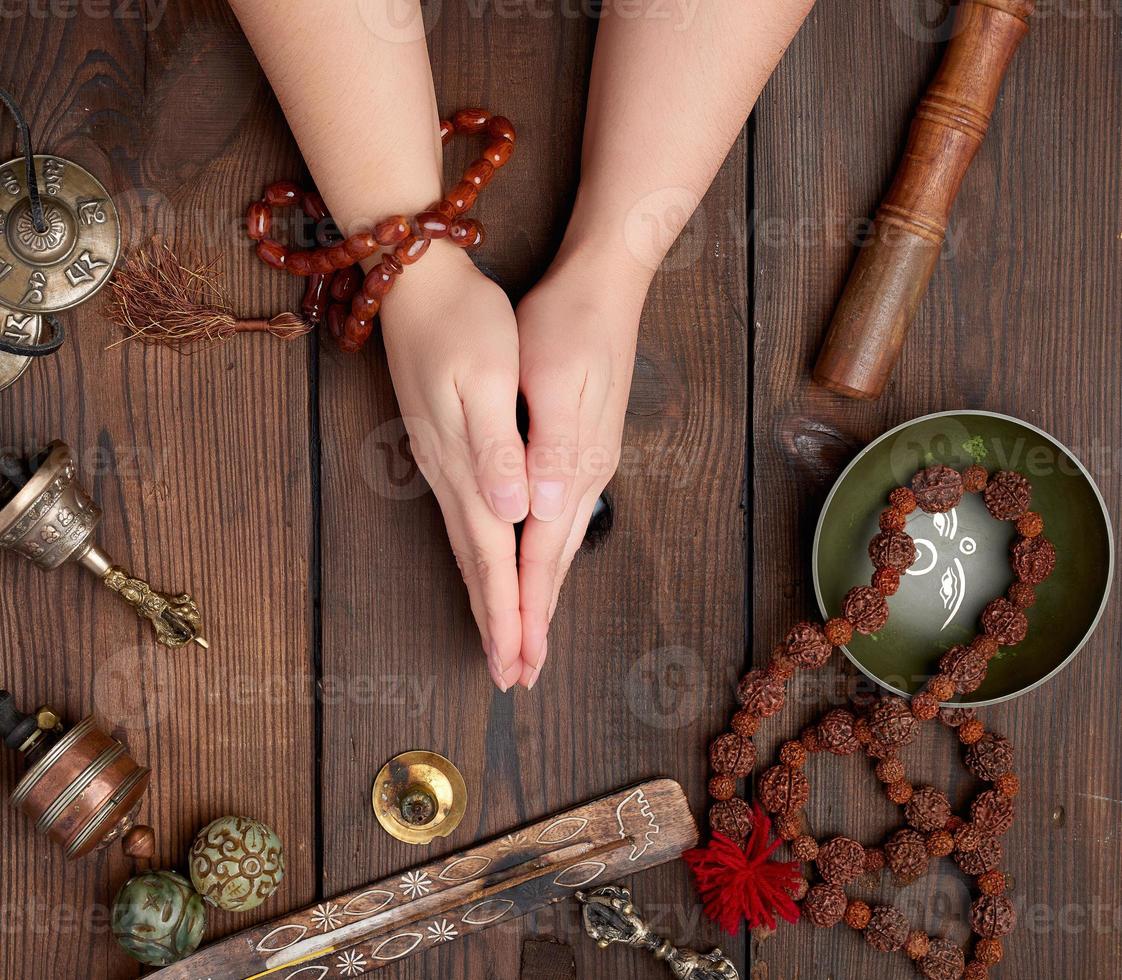 two hands in a prayer pose on a wooden brown table in the middle of vintage Tibetan meditation tools photo