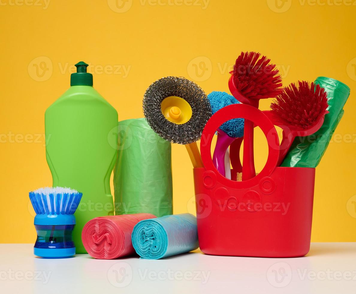 cesta de plástico con cepillos, desinfectante en una botella sobre fondo amarillo. foto