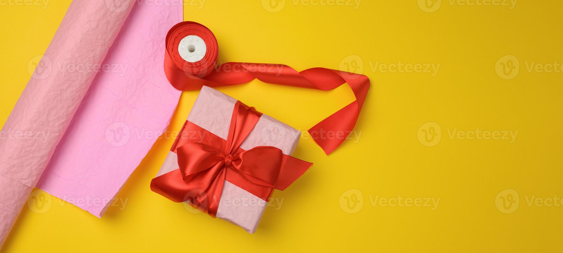 pink gift box wrapped in red silk ribbon on yellow background, top view photo