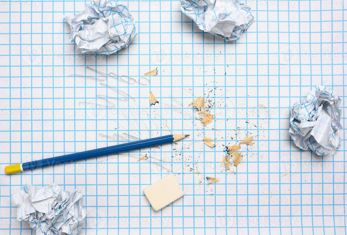 crumpled paper balls and a sharpened wooden pencil with shavings on a checkered paper sheet photo