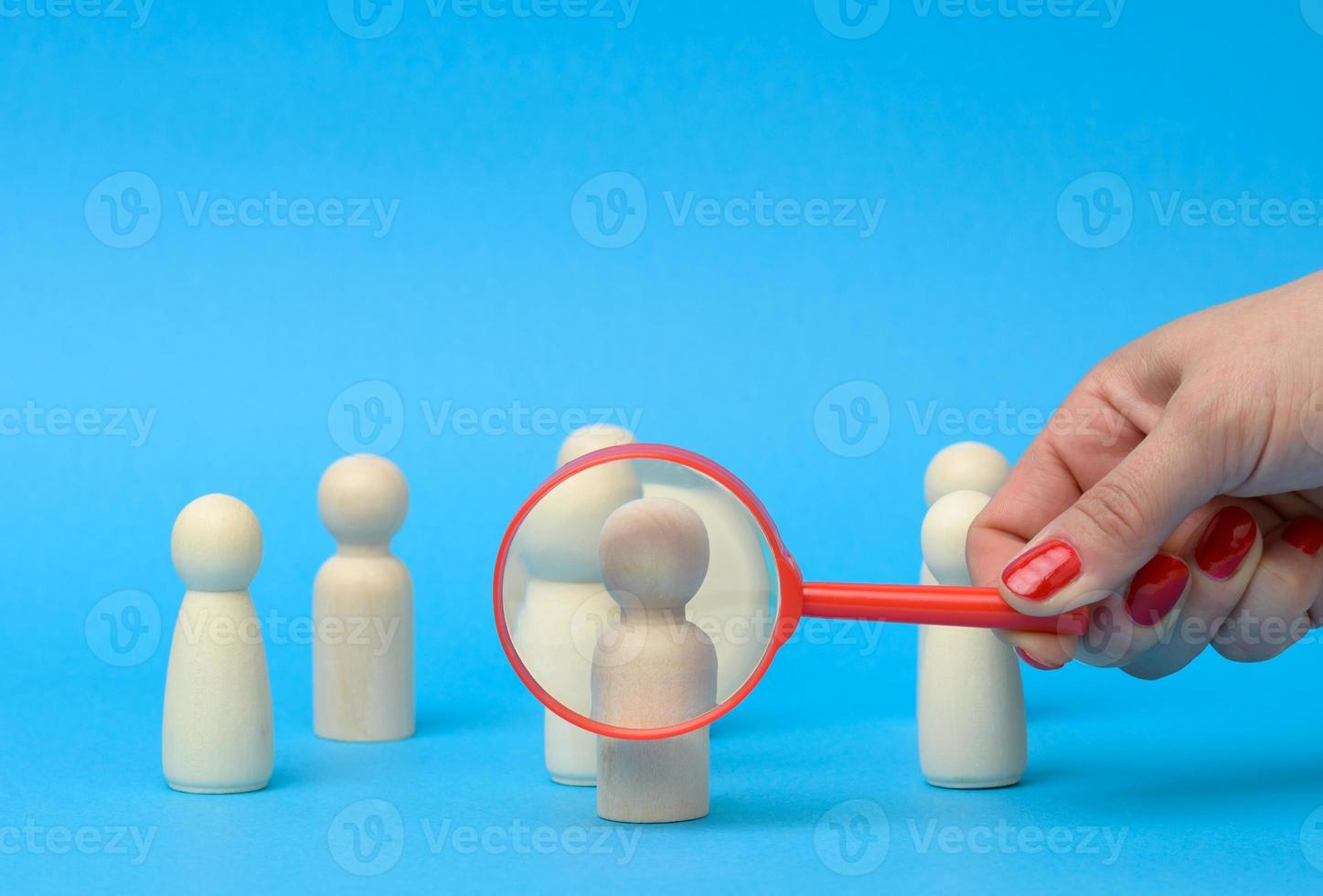 wooden figures of men stand on a blue background and a red magnifying glass photo