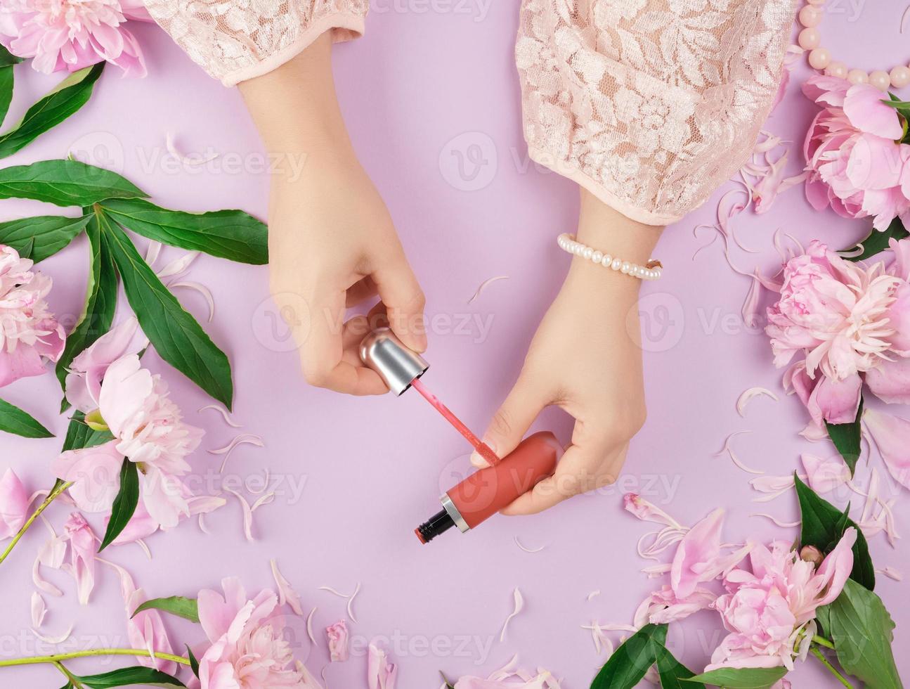 female hands with smooth fair skin keep liquid red lipstick in a tube photo