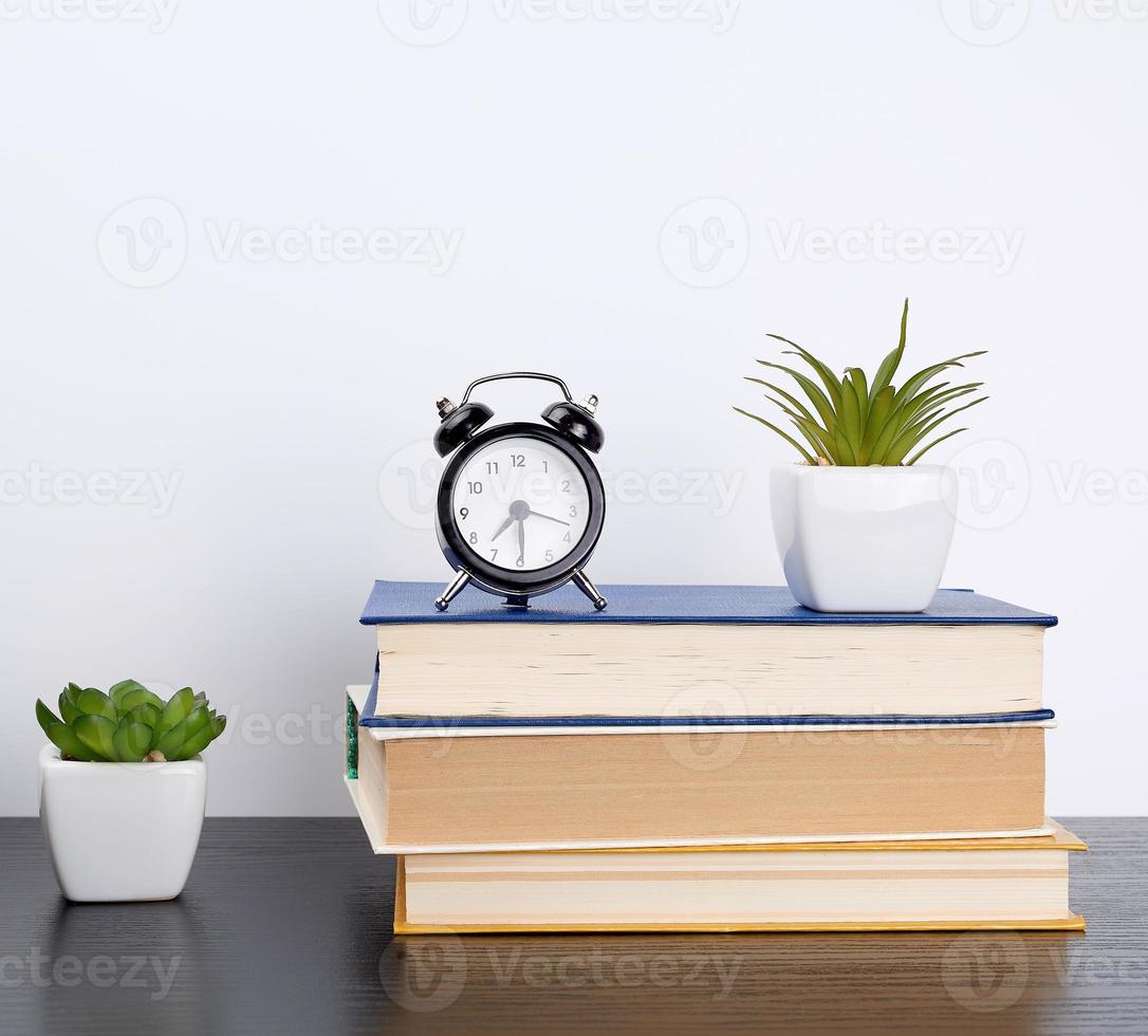 stack books on a black table, on top a ceramic pot with a green plant photo