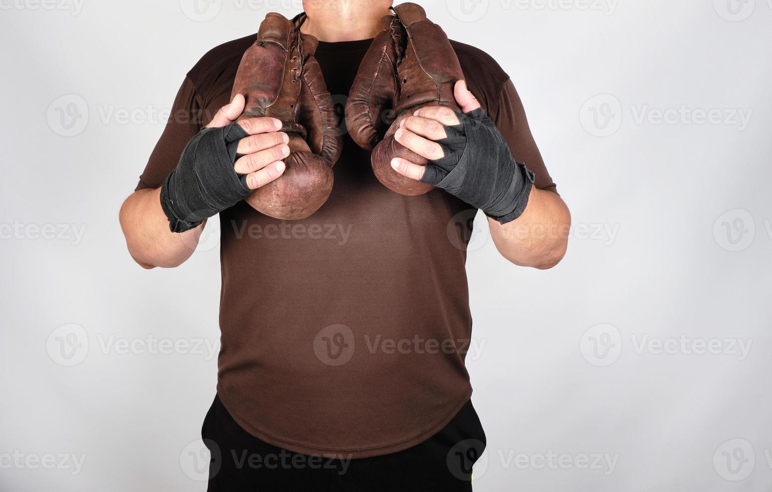 athlete in brown clothes holds very old vintage leather boxing gloves photo