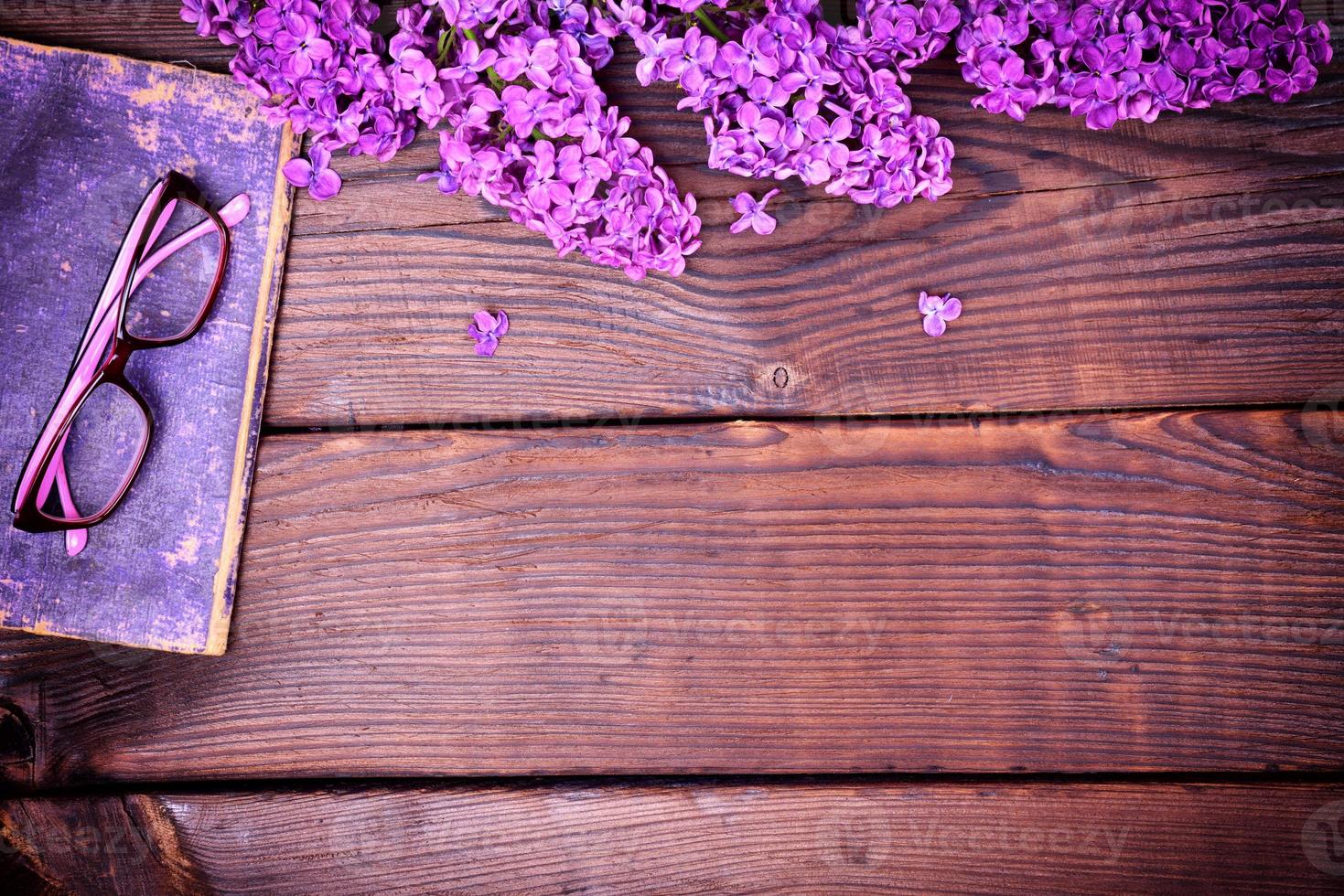 branch of a purple lilac and an old book with glasses photo