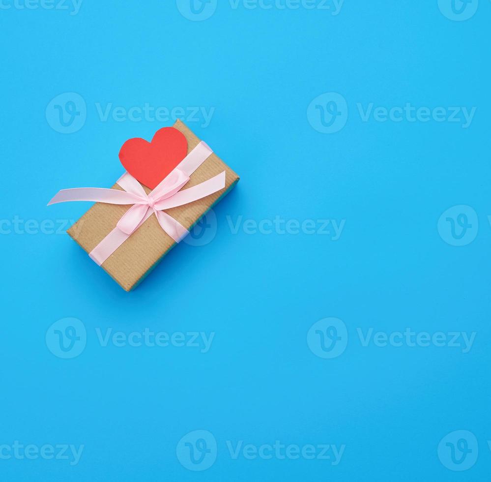 box is wrapped in brown paper and tied with a red thin silk ribbon on a blue background, red cut out paper hearts photo