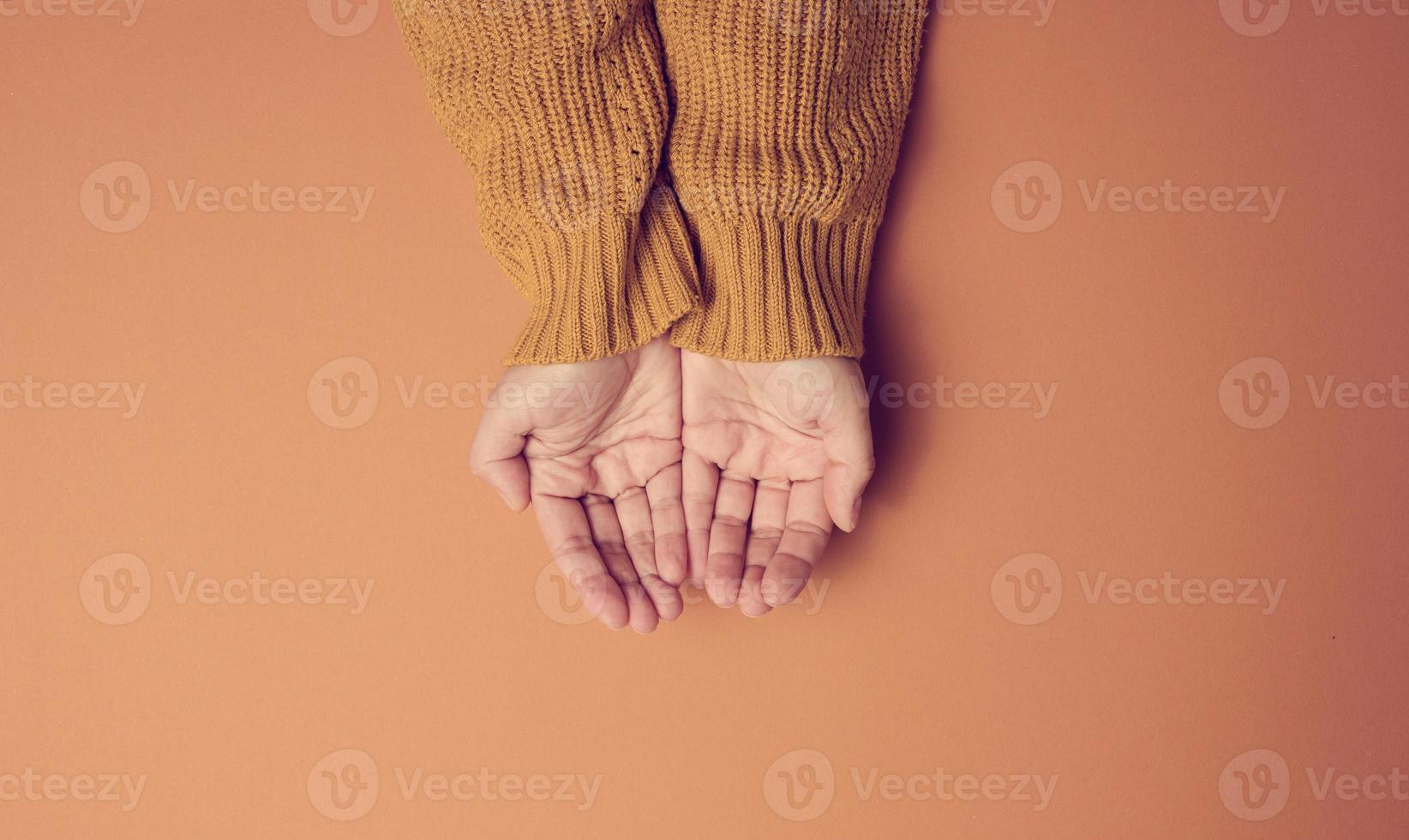two female hands folded palm to palm on an orange background, top view photo