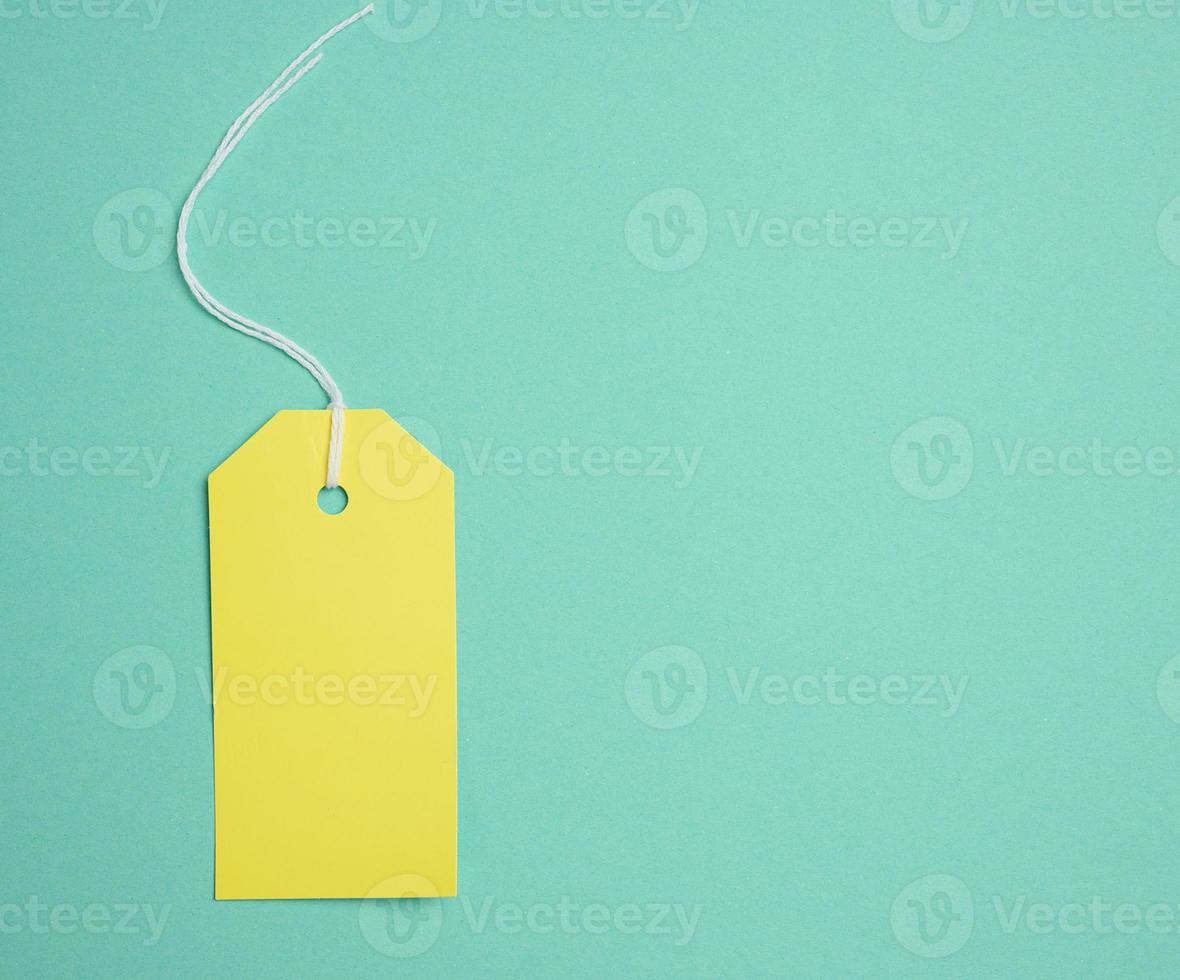 Empty yellow cardboard tag on a white rope, green background. Price tag template photo