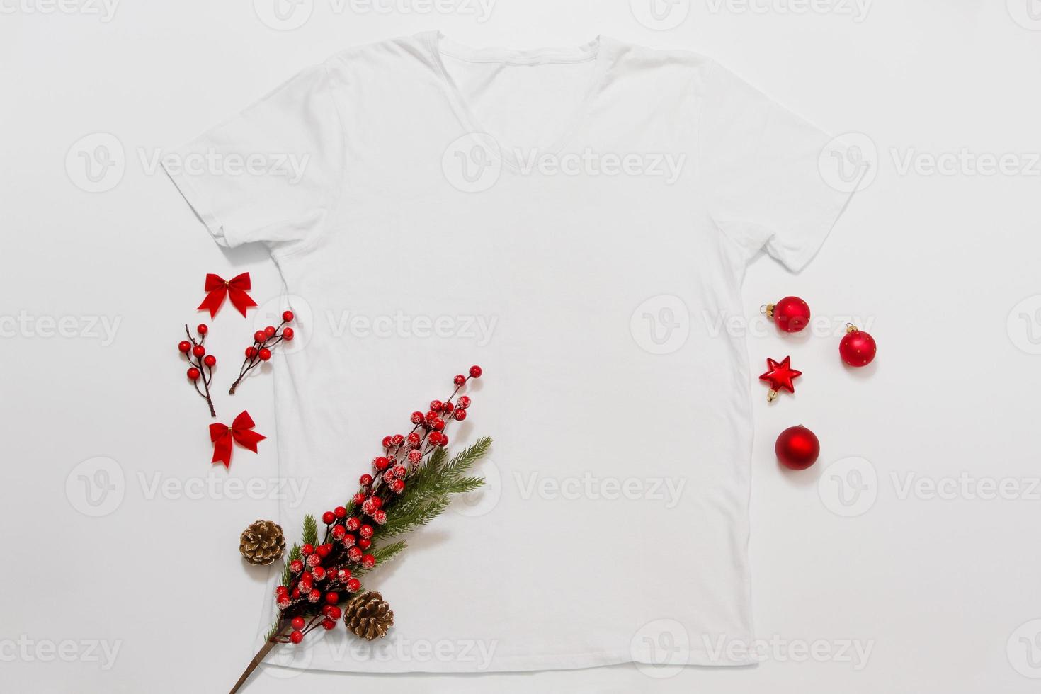 Close up white blank template t shirt with copy space and Christmas Holiday concept. Top view mockup t-shirt and red holidays decorations on white background. Happy New Year accessories. Xmas outfit photo