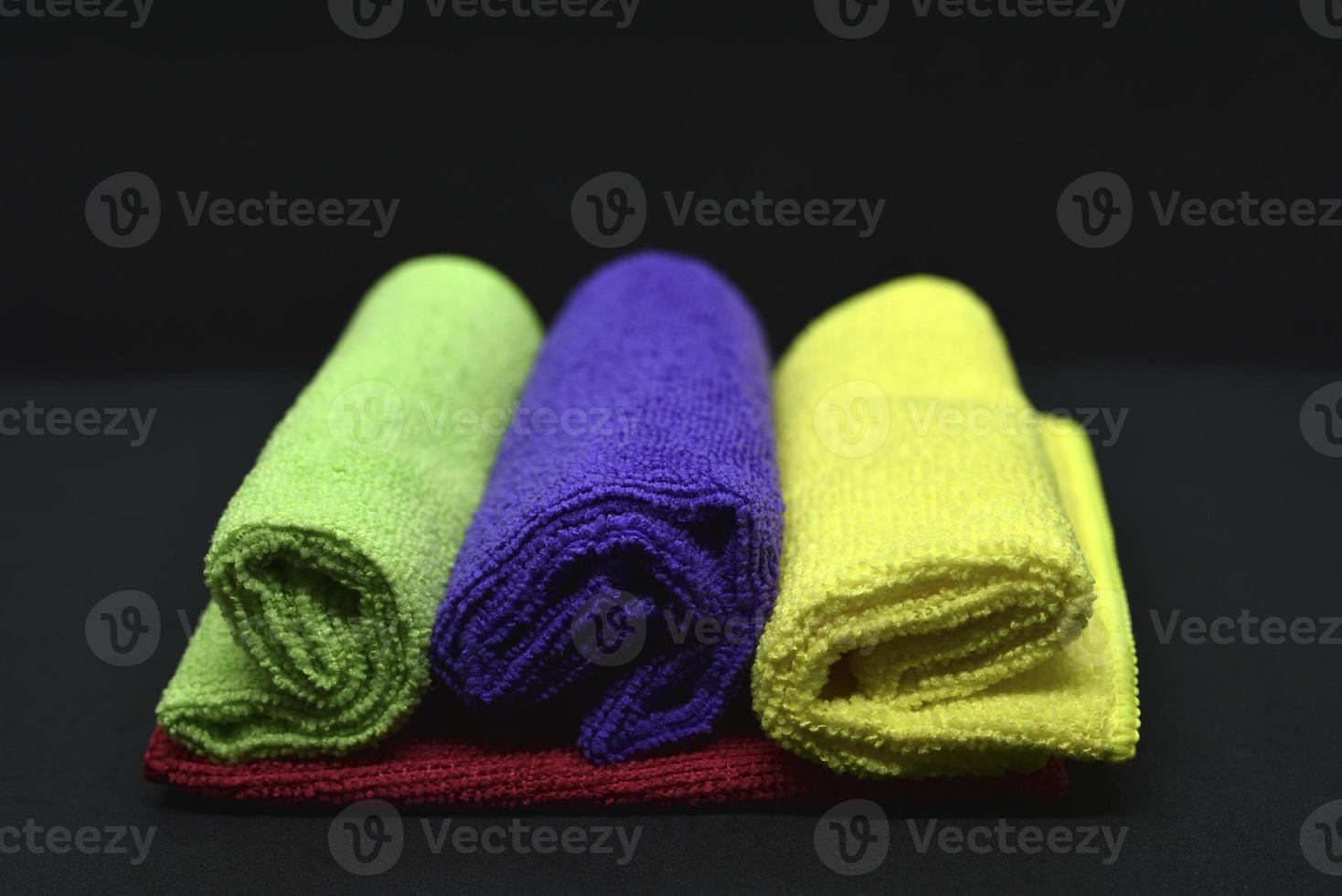 Multicolored towels on a black background. Terry towels. Colored rags in rolls. Rolled-up rags. photo