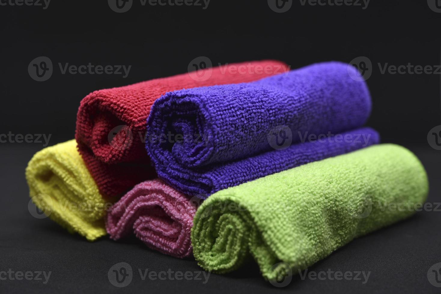 Multicolored towels on a black background. Terry towels. Colored rags in rolls. Rolled-up rags. photo