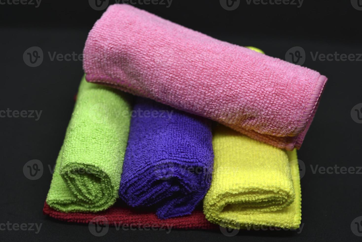 Multicolored towels on a black background. Terry towels. Colored rags in rolls. Rolled-up rags. photo