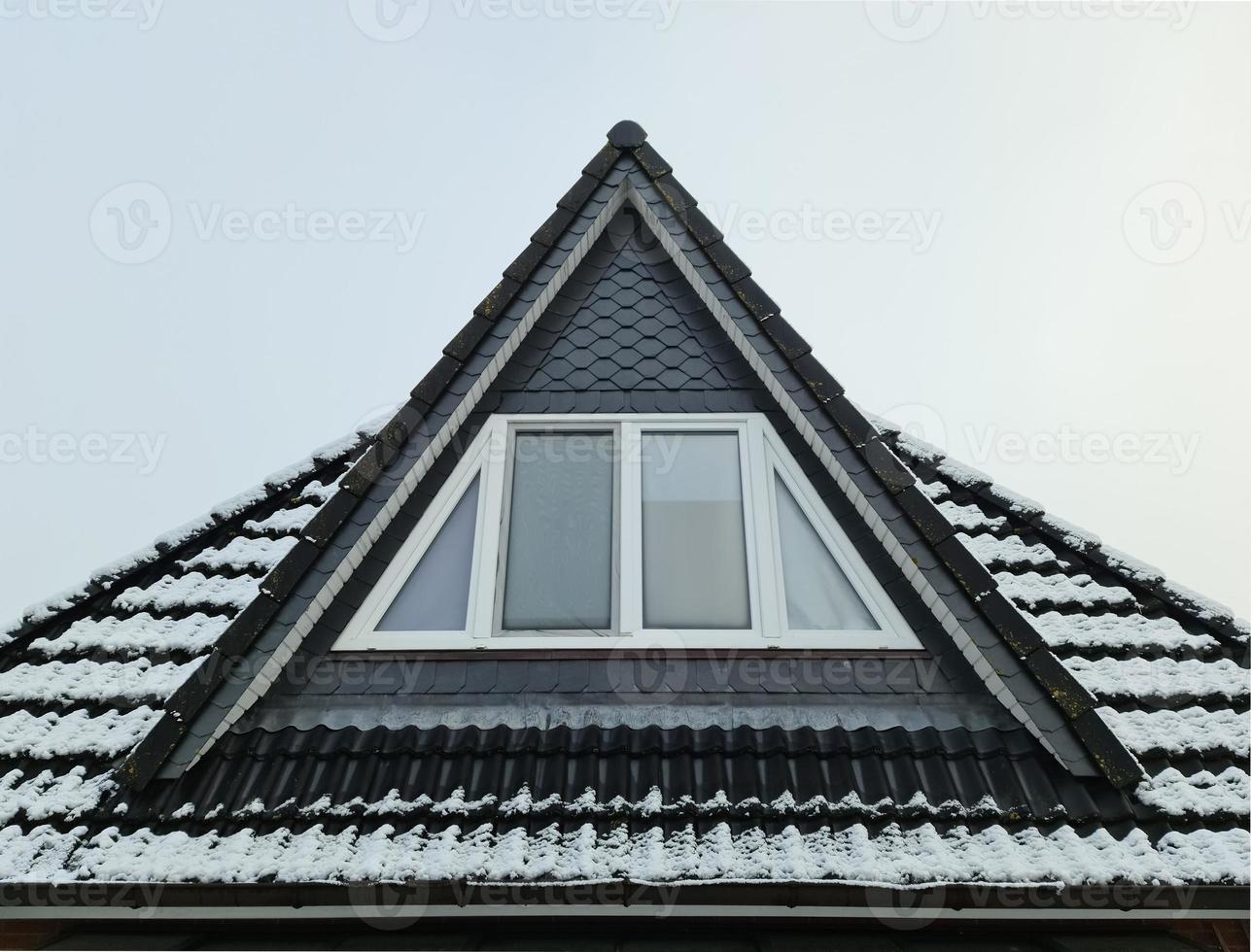 Open roof window in velux style with black roof tiles covered in white snow photo