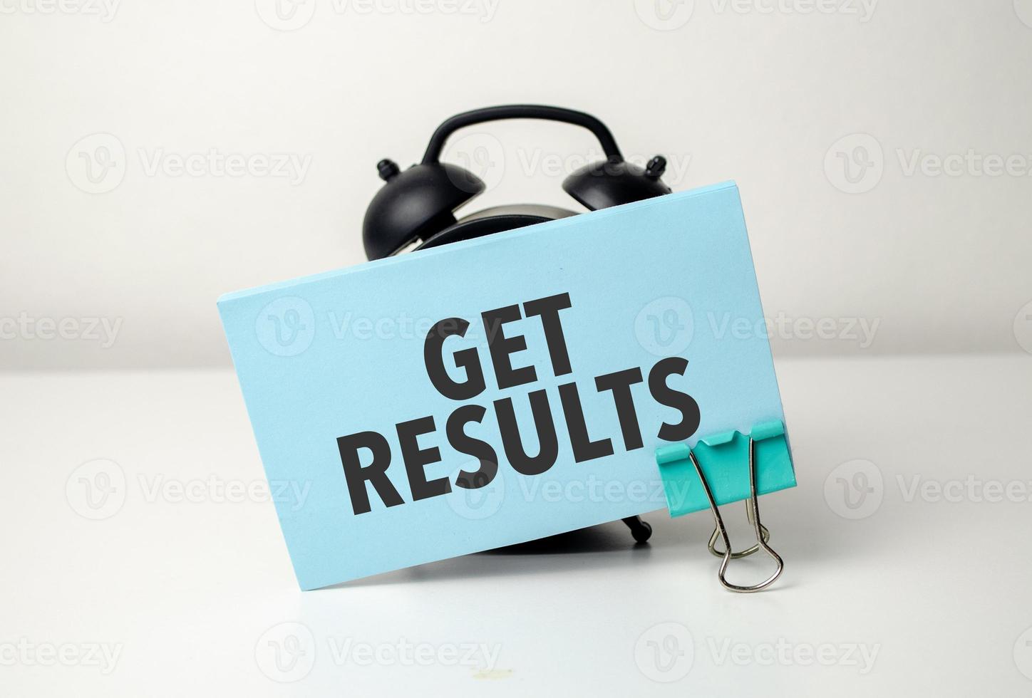 get results is written in a blue sticker near a black alarm clock photo