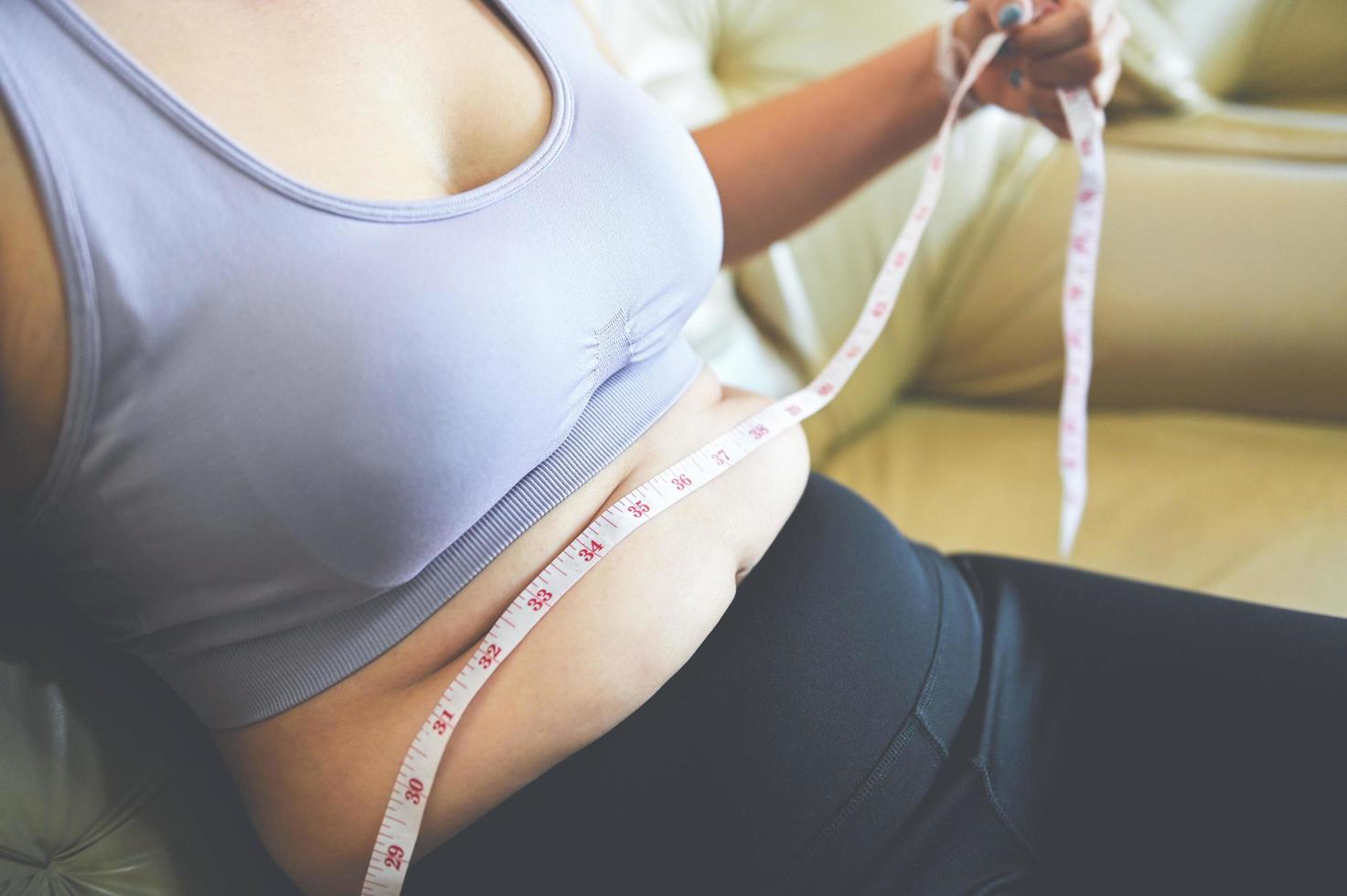 mujer gorda midiendo, mujer gorda gorda barriga gordita deporte recreación cuidado de la salud perder el concepto de grasa abdominal, mujer sosteniendo barriga excesiva con cinta métrica foto