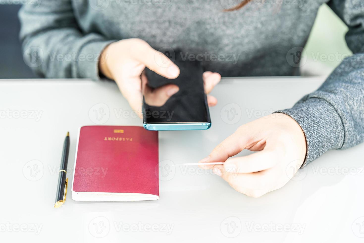 Woman sitting and using smartphone for online shopping with credit card and passport on deck in home office photo