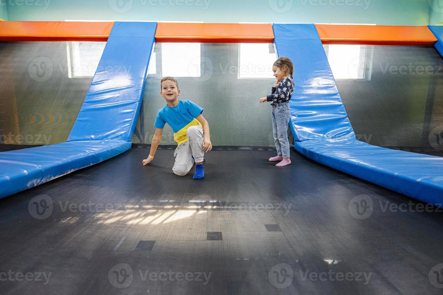 Brother with sister playing at indoor play center playground , jumping in trampoline. photo