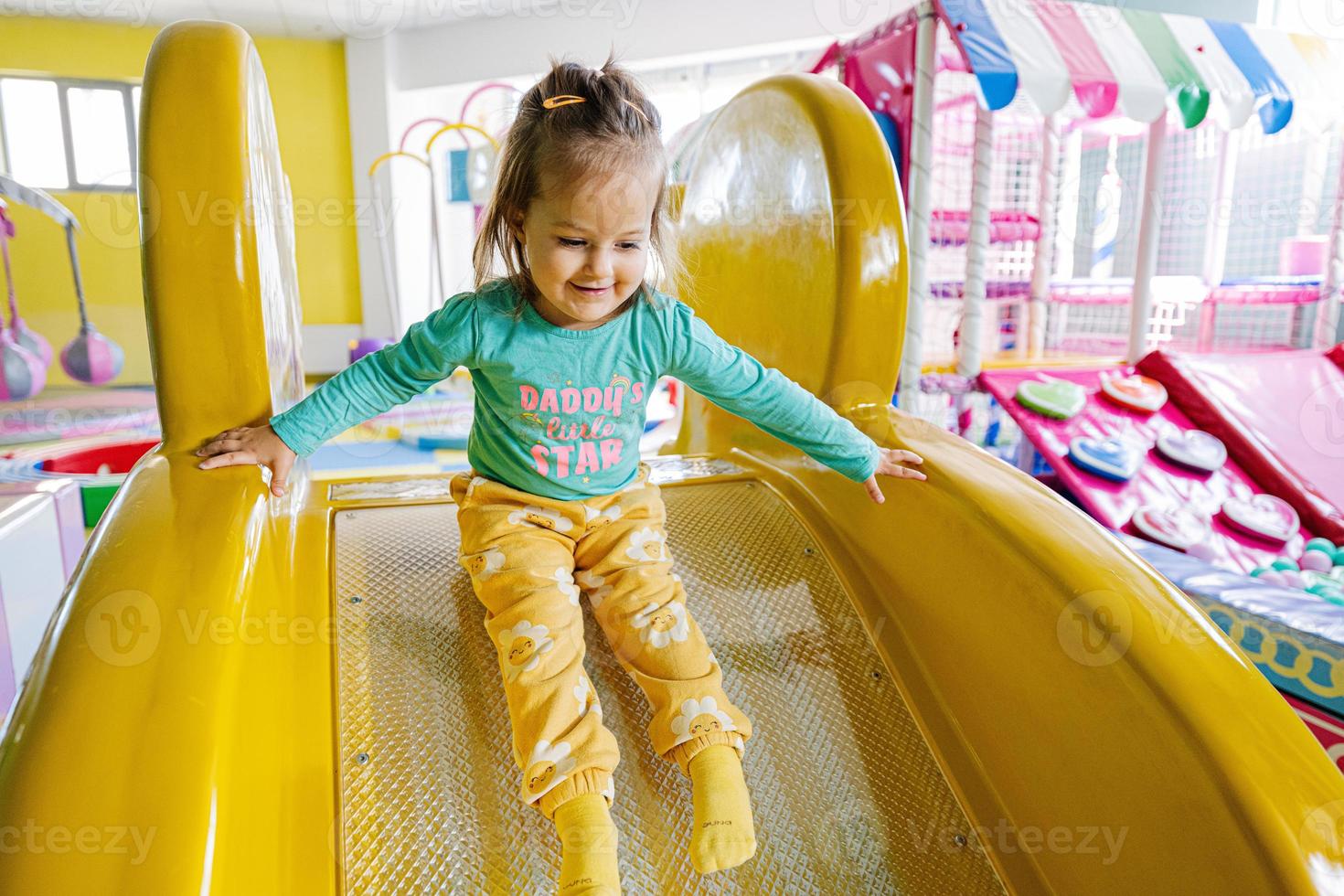Happy girl playing at indoor play center playground. Sliding in yellow slide. photo