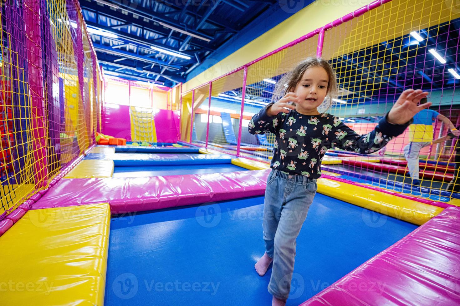Happy kids playing at indoor play center playground. Girl jumping on trampoline. photo