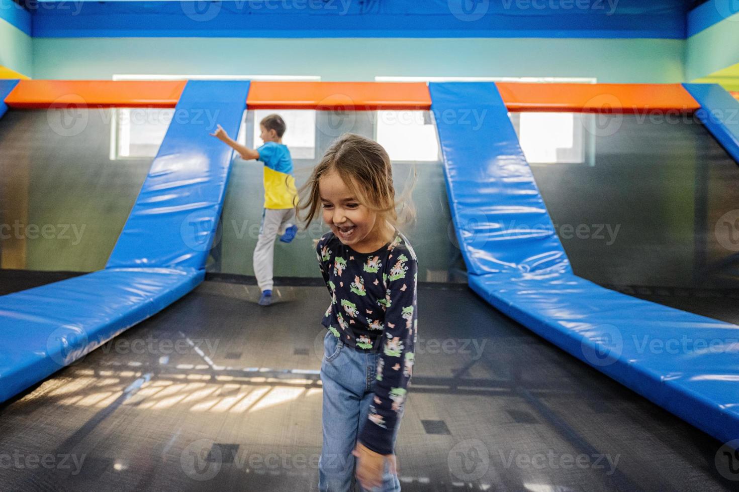 Brother with sister playing at indoor play center playground , jumping in trampoline. photo