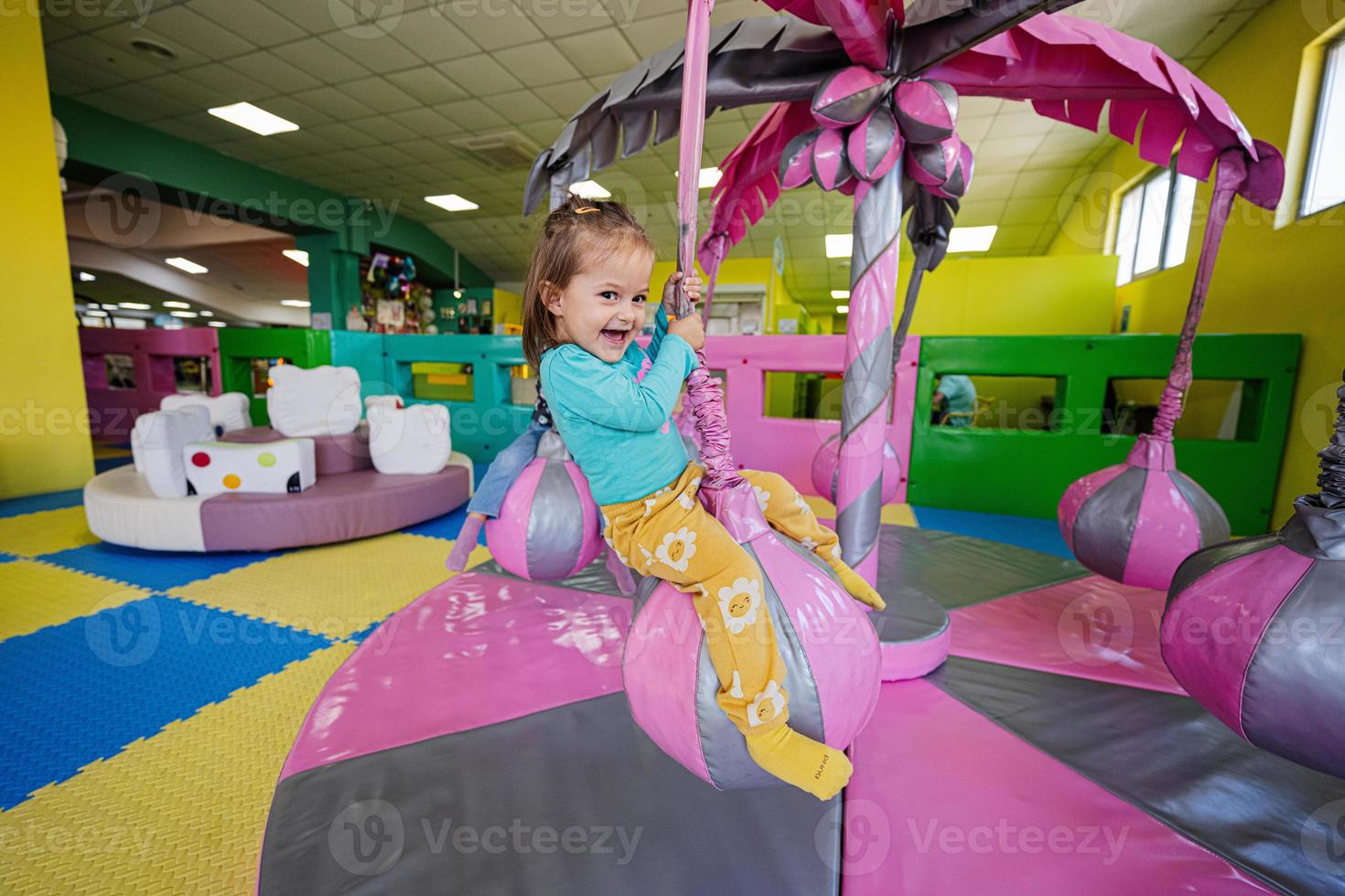 Happy girl playing at indoor play center playground,  swing on palm. photo