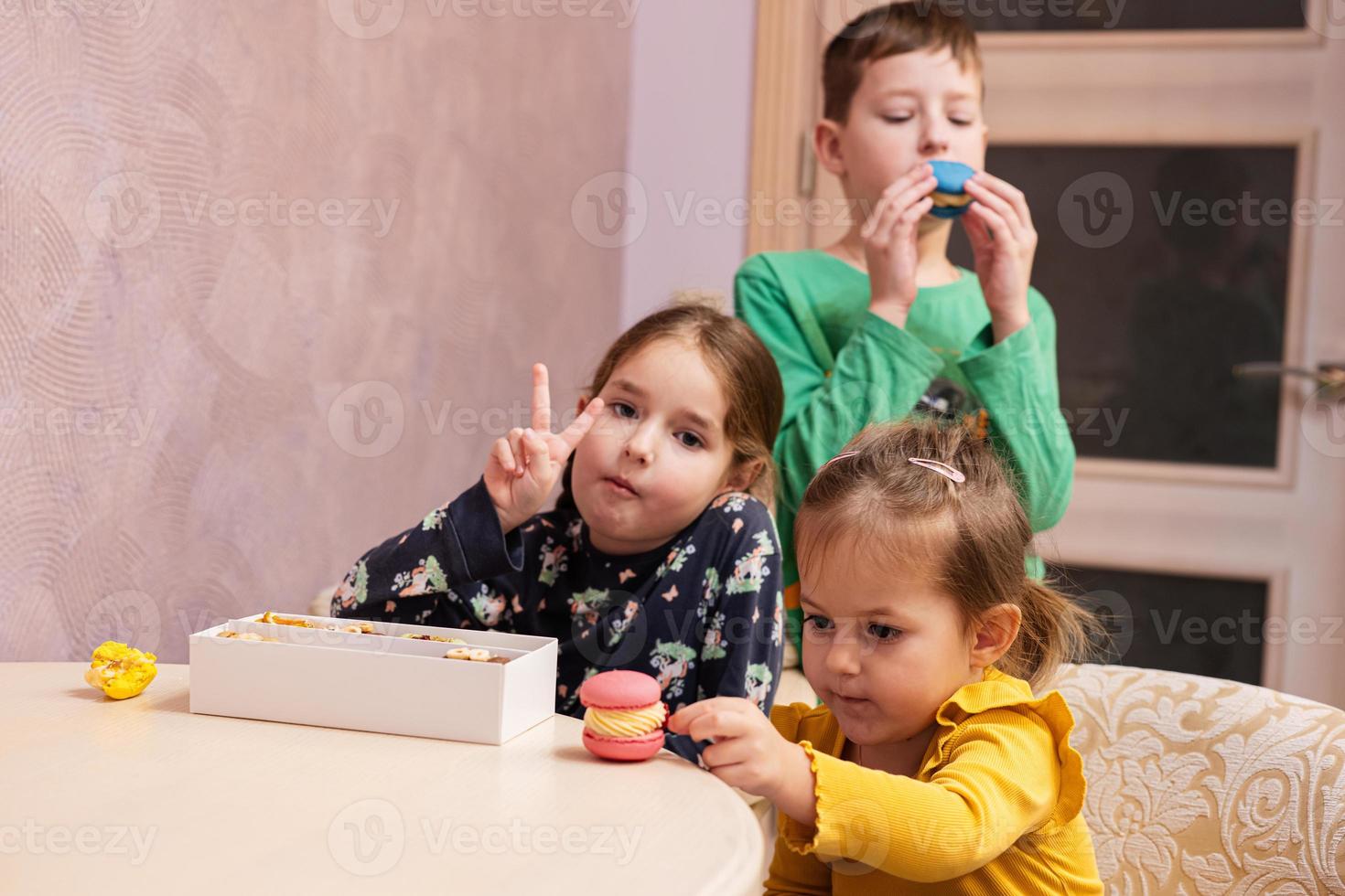 Three kids eat delicious tasty sweet color macarons. photo