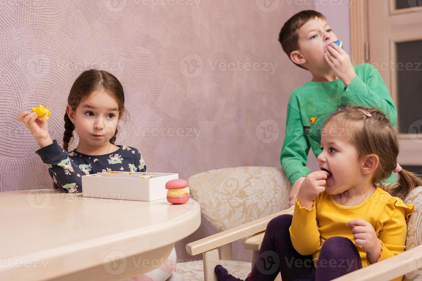 Three kids eat delicious tasty sweet color macarons. photo