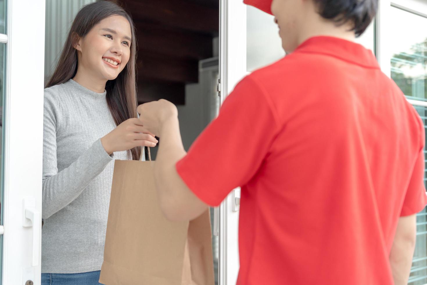 Happy smiling Asian woman receives paper bag parcel of food from courier front house. Delivery man send deliver express. online shopping, paper container, takeaway, postman, delivery service, packages photo