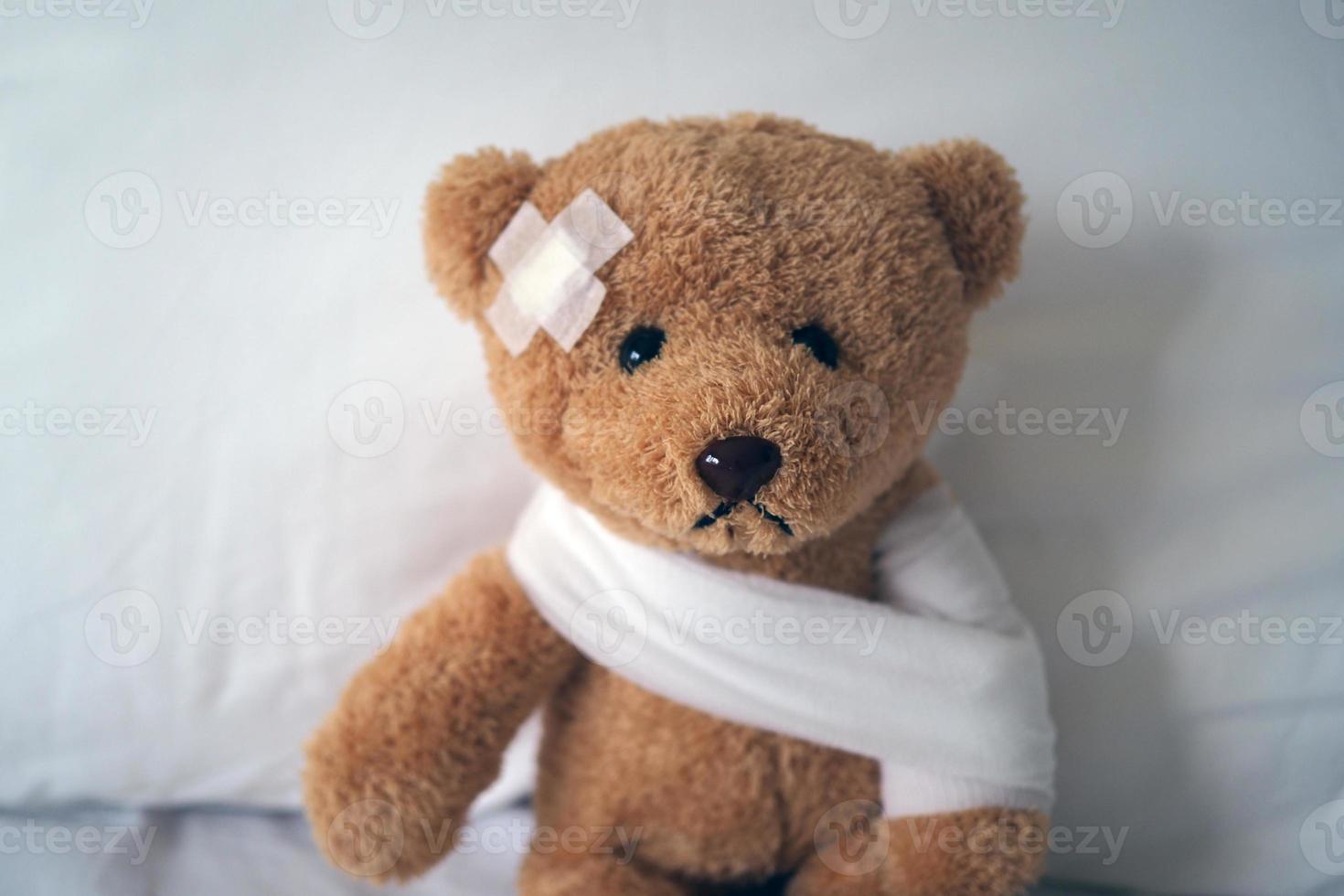 Sad bear doll lying sick in bed with the wound on the head and bandage photo