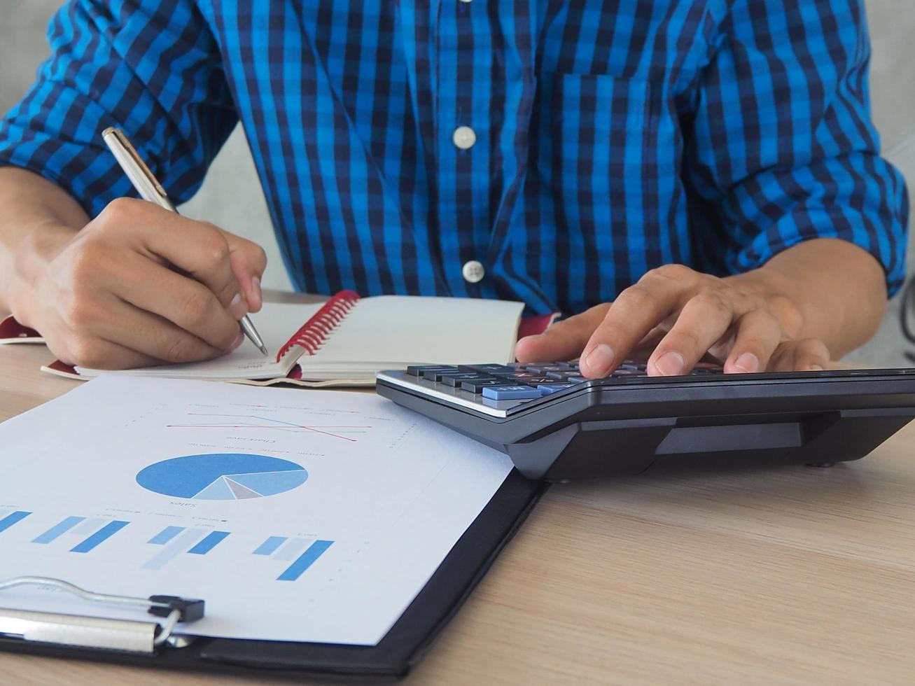 la mano de los hombres usa una calculadora para calcular estadísticas. sobre su trabajo y escribe la información en el libro. foto