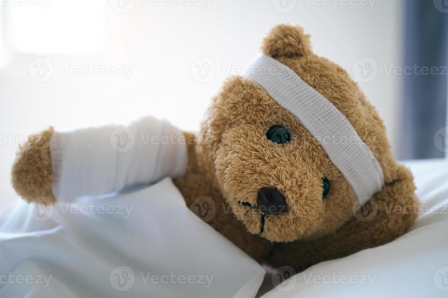 oso de peluche acostado enfermo en la cama con una diadema y un paño cubierto foto