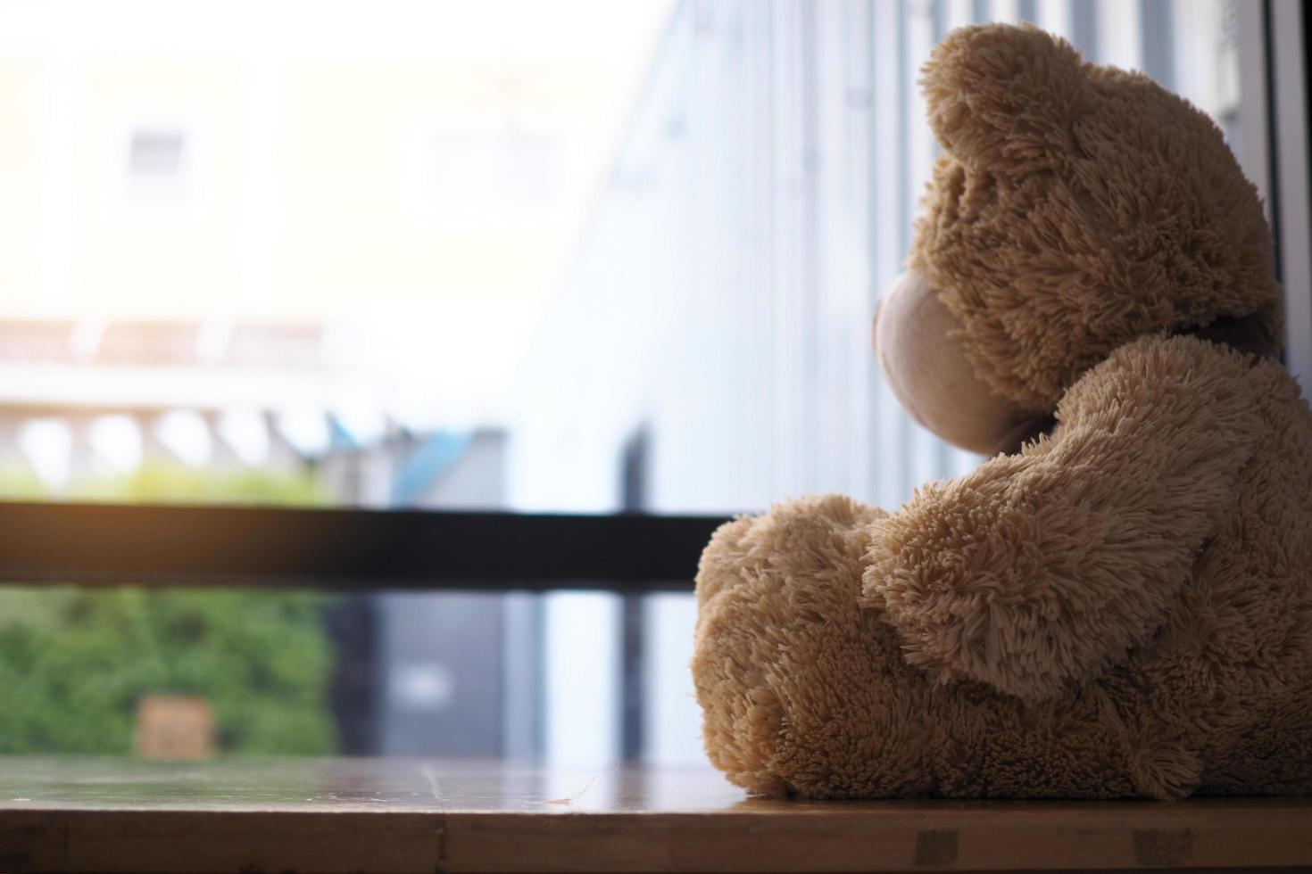 major depressive disorder mdd concept. Grief of children. Teddy bear sitting looking at the house window alone. Looks like someone who is sad, disappointed, depressed photo