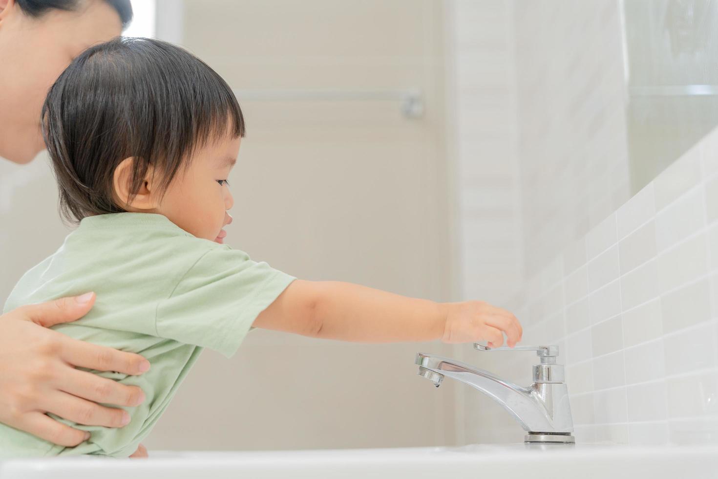 Little kid hand closed the faucet at sink in house with mom. Mother teaches child to save water. keeps turning off the water to save world energy and protect the environment, world water day photo