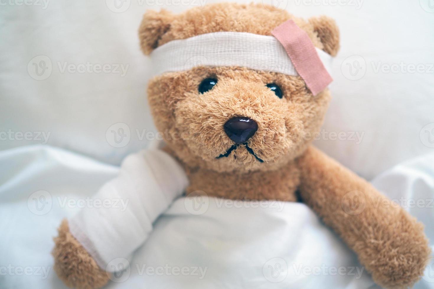 Teddy bear lying sick in bed With a headband and a cloth covered photo