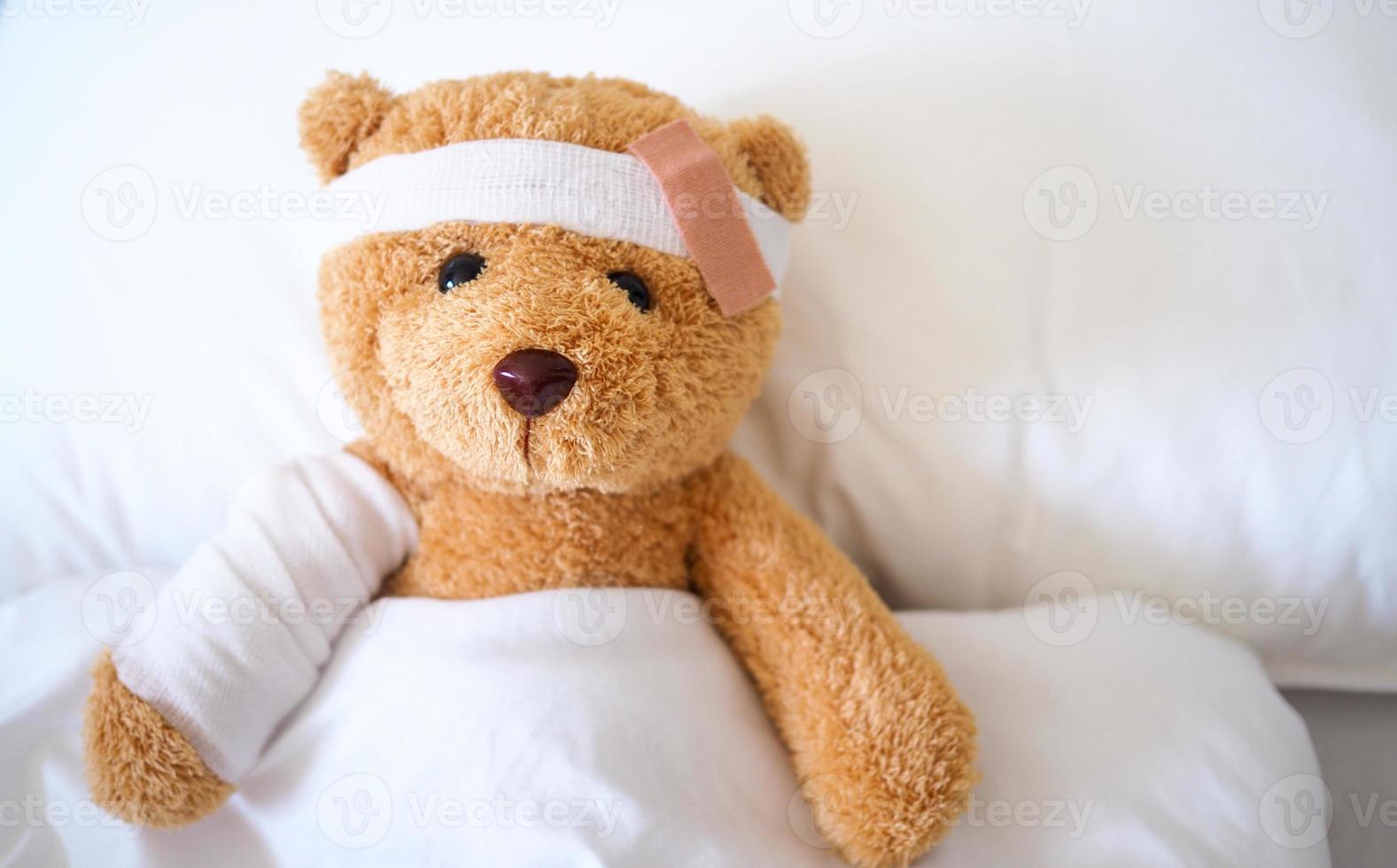 Teddy bear lying sick in bed With a headband and a cloth covered photo