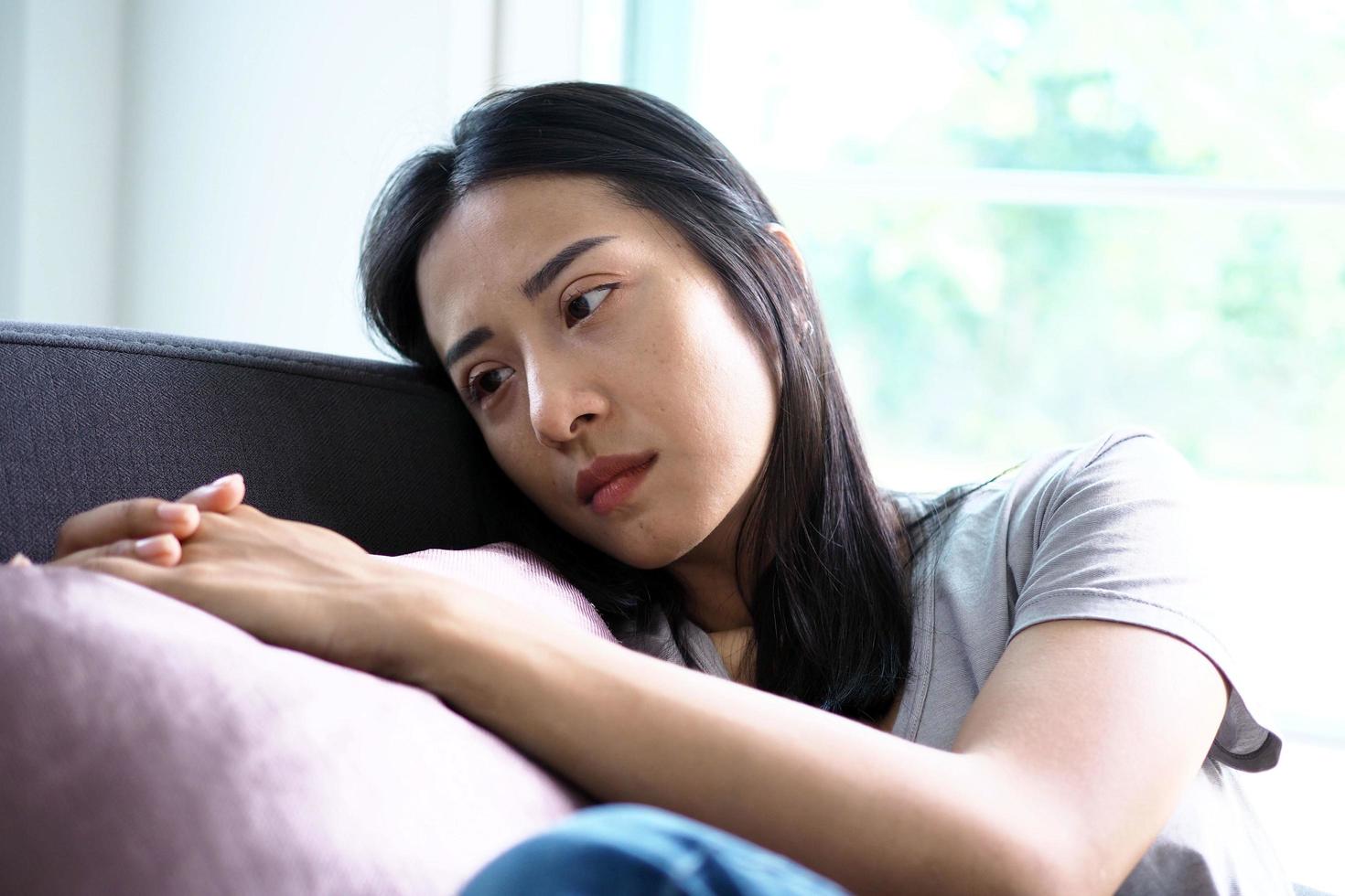 A beautiful Asian middle-aged woman has a sad and depressed expression on the couch in the house. photo
