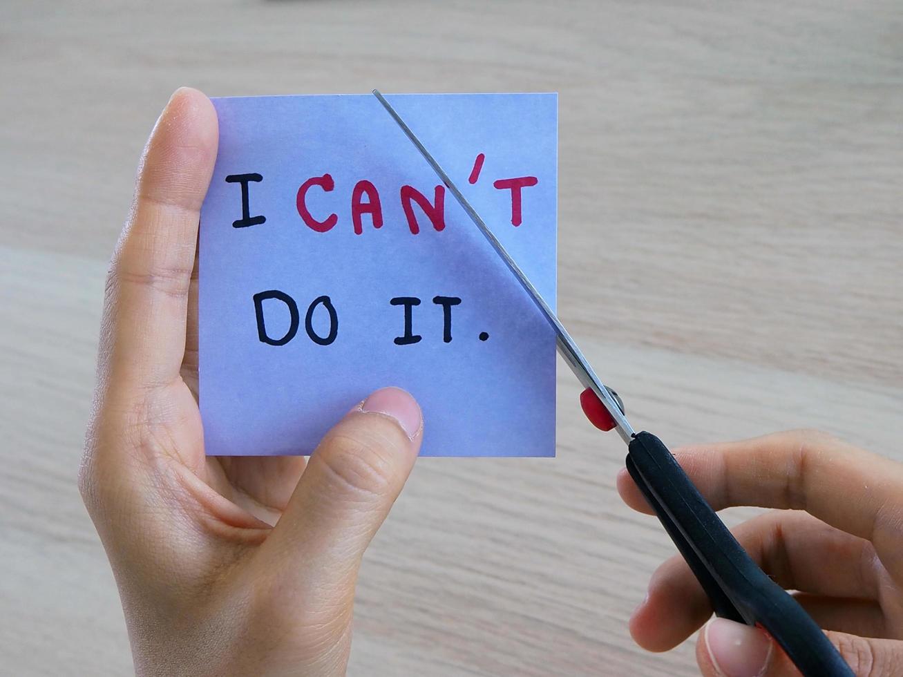 la mano de una mujer sostiene una nota con el mensaje que escribió cuando no tenía la intención. y ahora usa las tijeras para cortar la letra t porque se inspiró en algo. foto