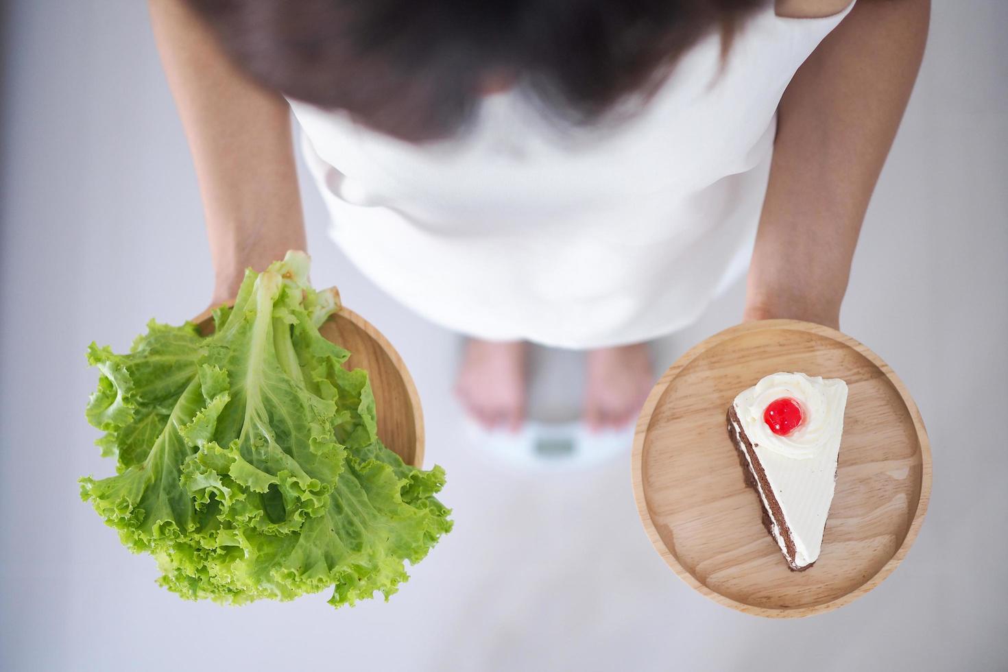 Female holding vegetable dishes and cakes thinking of choosing to eat which is more beneficial to the body. Weight loss concept, eating things that make healthy photo