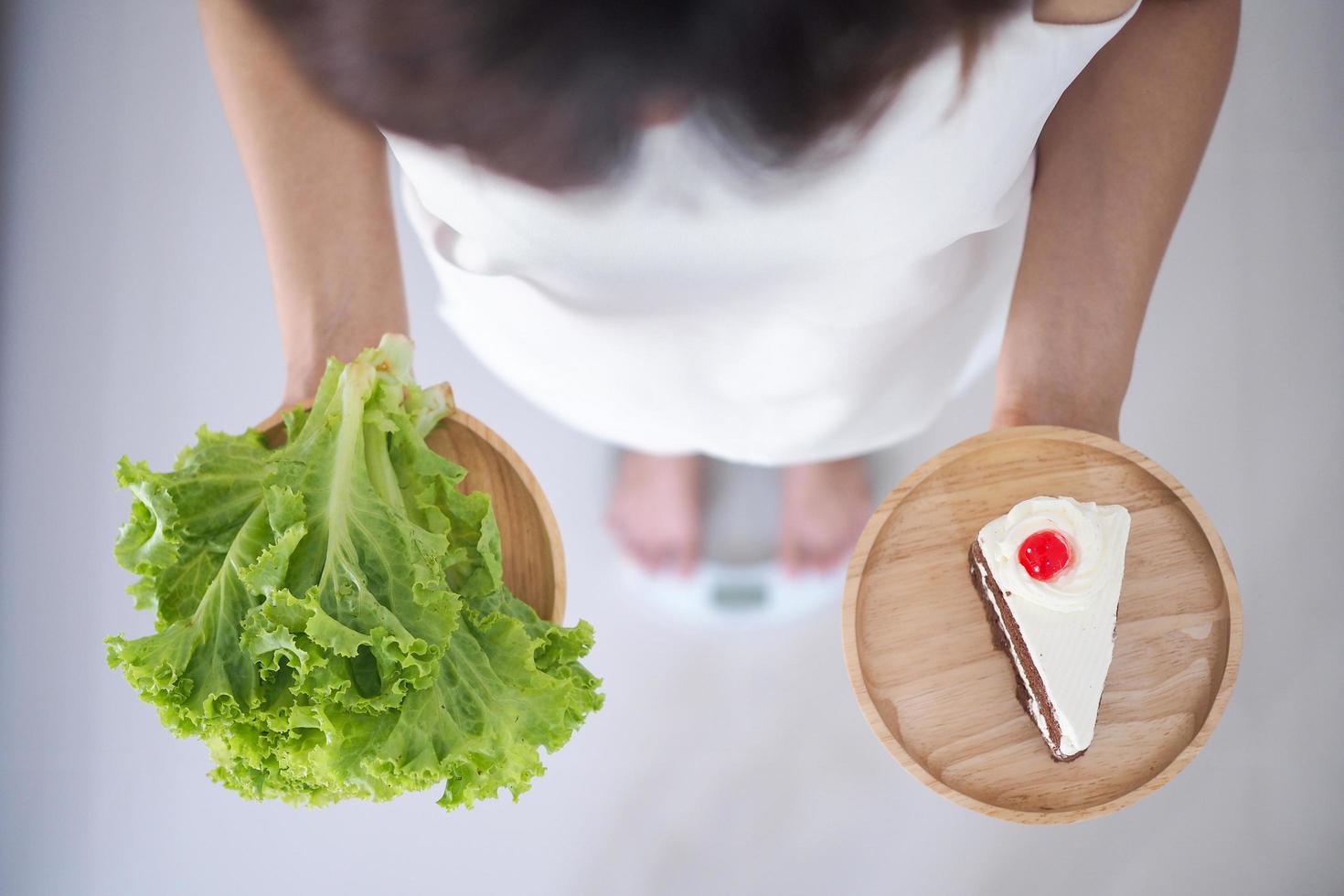 mujer sosteniendo platos de verduras y pasteles pensando en elegir comer lo que es más beneficioso para el cuerpo. concepto de pérdida de peso, comer cosas que hacen saludable foto