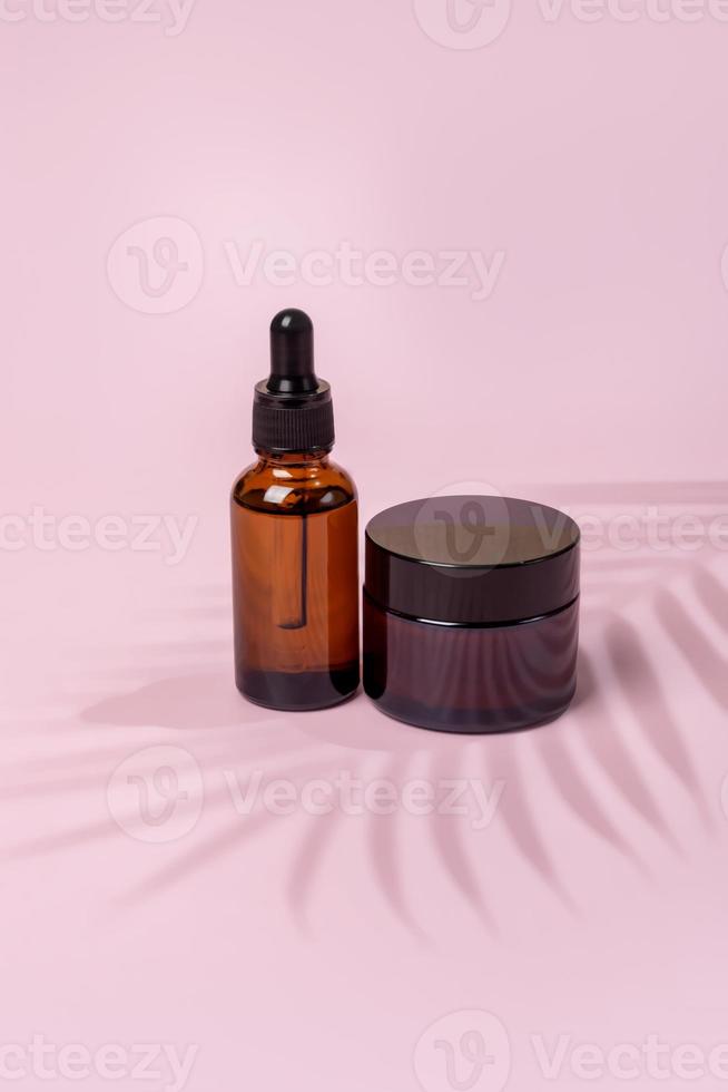 conjunto de productos para el cuidado de la piel en un paquete en blanco de vidrio ámbar sobre fondo rosa. concepto de tratamiento facial y corporal. cosmética natural, maqueta con sombra de palmera foto