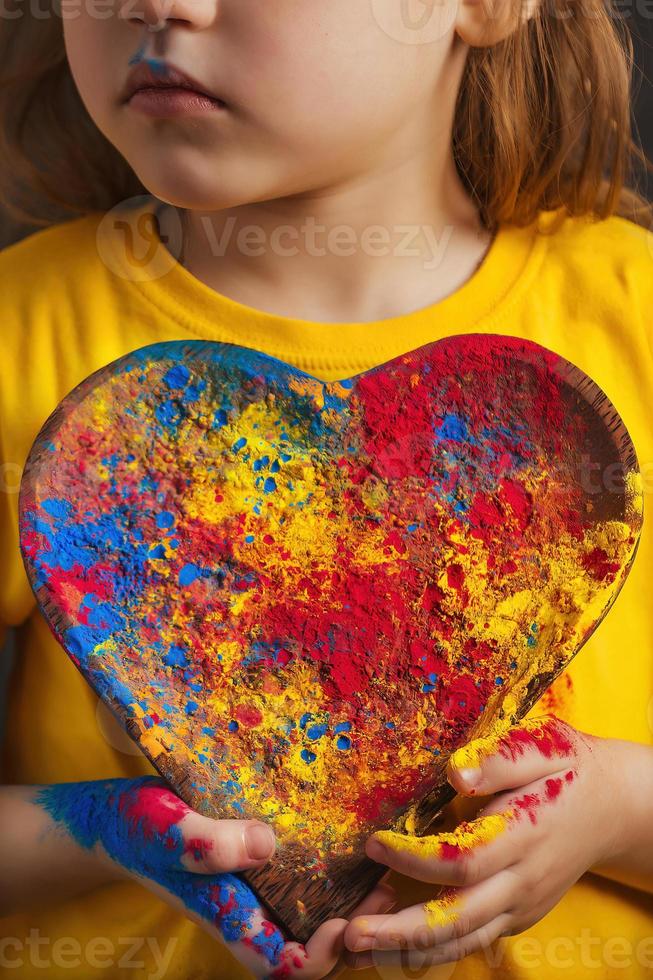 children's hands hold a wooden plate in the shape of a heart in which the multi-colored bright colors of Holi. Indian festival of colors Holi. photo