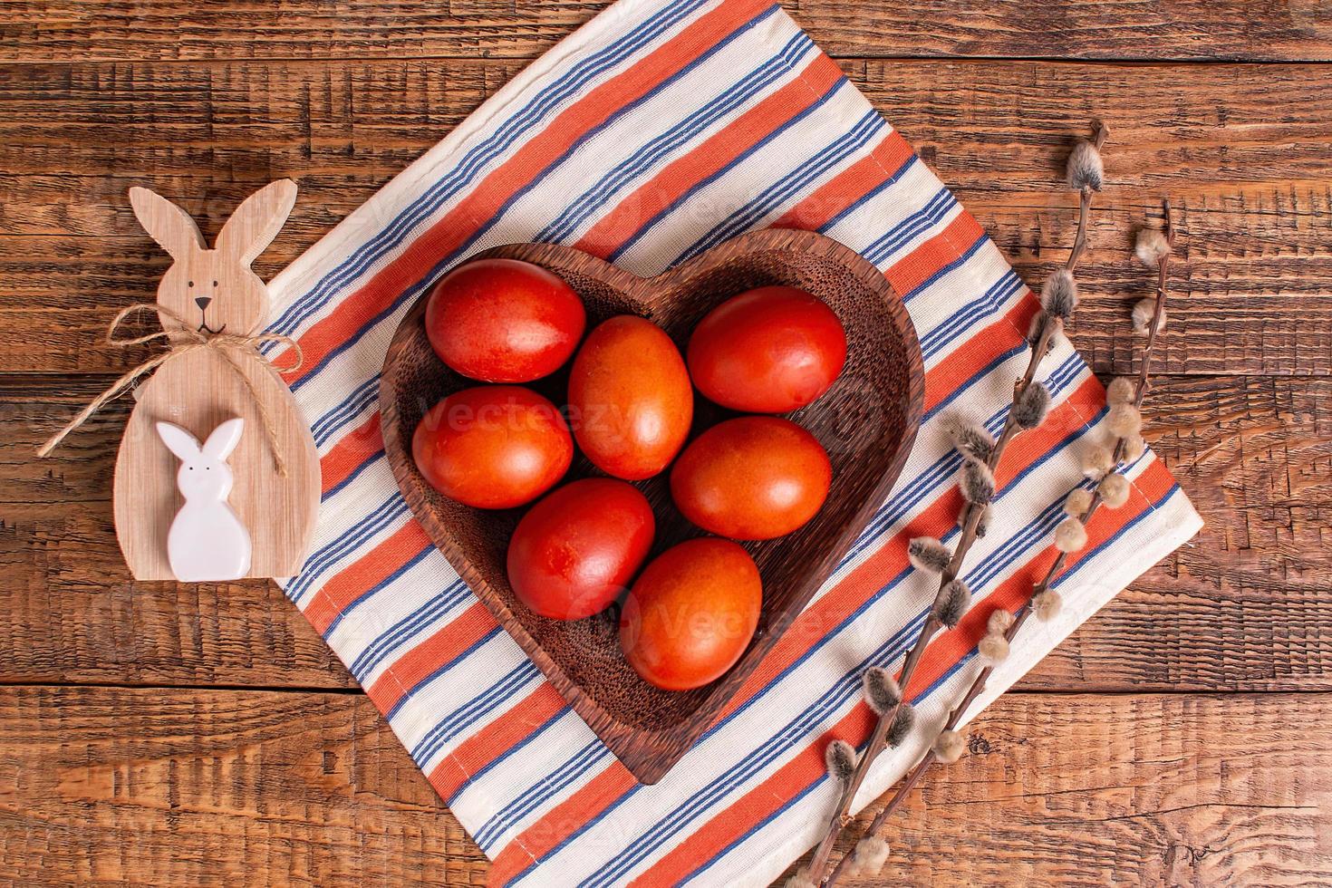 on a wooden background Easter eggs painted with natural vegetable paints with onion peel, next to a wooden Easter rabbit and willow top view, preparation for the Easter holiday photo