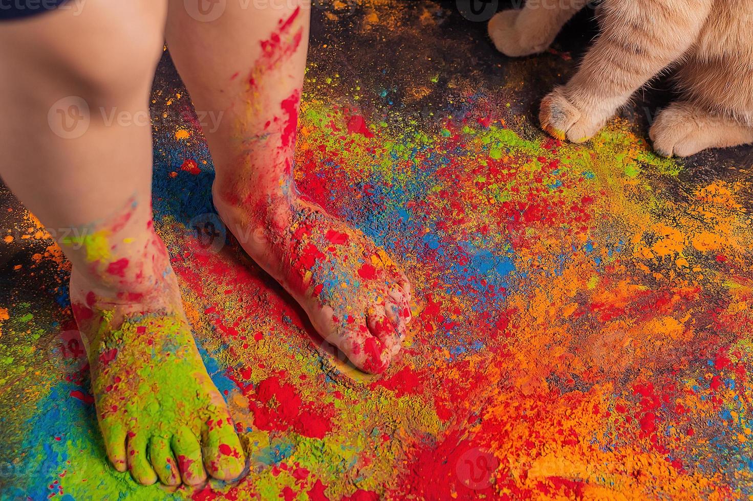 children's feet strewn with multi-colored bright Holi colors and cat paws nearby, copy space. Indian festival of colors Holi. photo