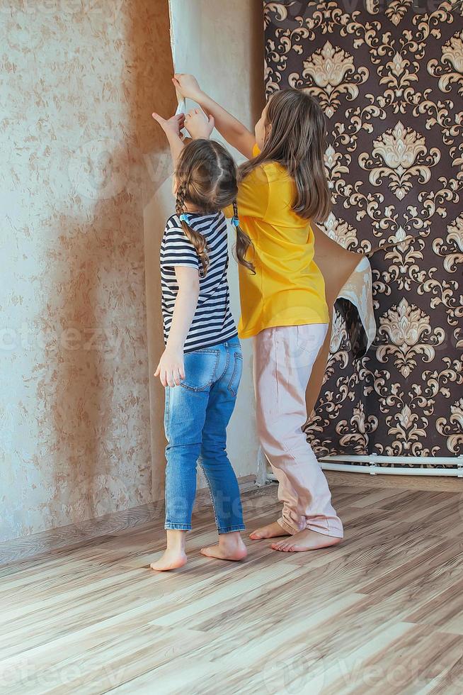 la familia hace las reparaciones con sus propias manos, dos hermanas quitan juntas el papel tapiz viejo de las paredes y ayudan a sus padres con las tareas domésticas. foto