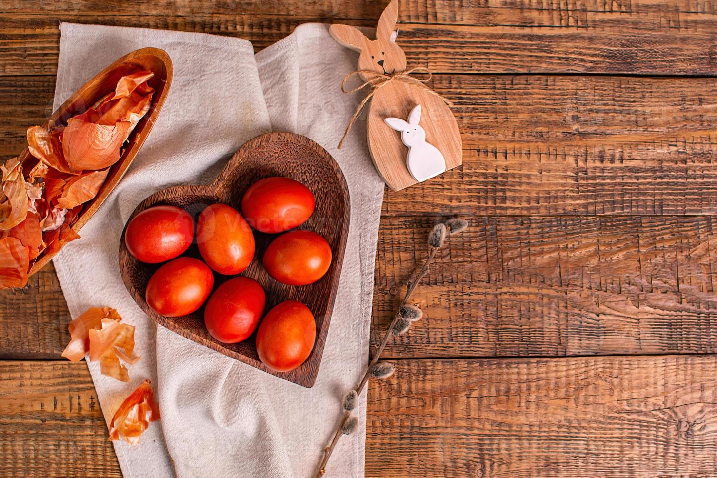 sobre un fondo de madera huevos de pascua pintados con pinturas vegetales naturales, cáscara de cebolla, junto a un conejito de pascua de madera y sauce, vista superior, espacio para copiar foto