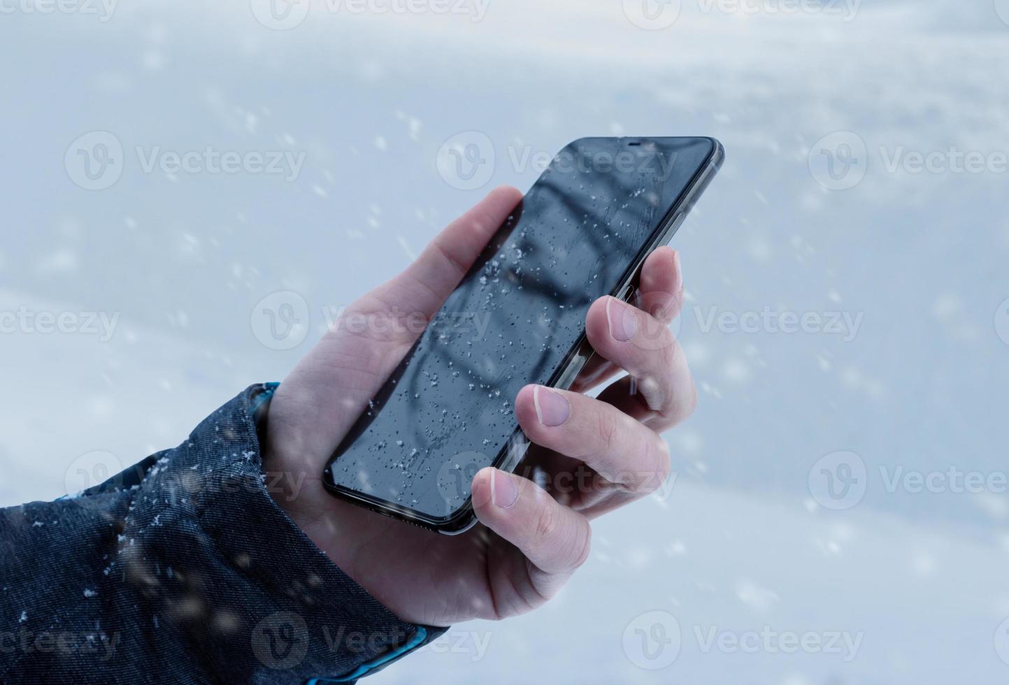 Phone in a man's hand. Snowing on the hand and the device. Snow, winter, cold weather photo